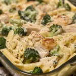 A golden, bubbly casserole dish of Chicken and Broccoli Baked Alfredo with a creamy Alfredo sauce.